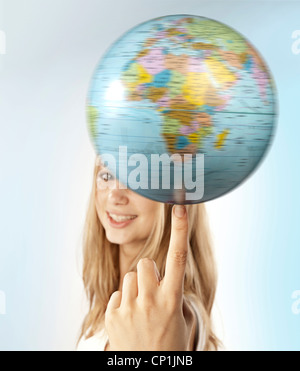 Young woman balancing a globe on her finger. Stock Photo
