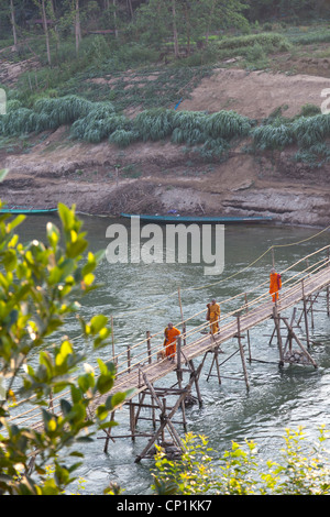 Novice monks using the flimsy bamboo footbridge thrown across the Khan river, a tributary of the Mekong (Luang Prabang - Laos). Stock Photo