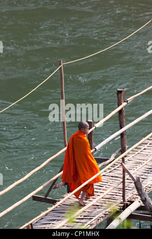 A monk using the bamboo footbridge thrown across the Khan river, a tributary of the Mekong (Laos). Moine sur une passerelle. Stock Photo