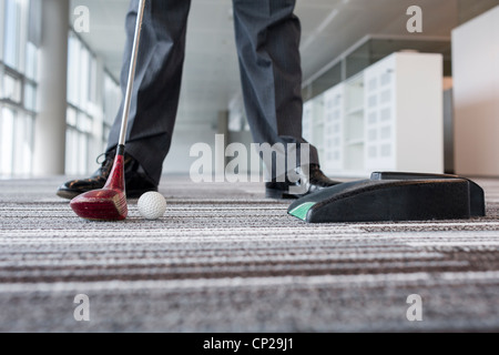 Businessman playing golf in empty office space Stock Photo