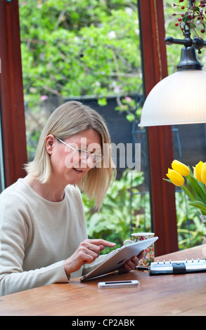 Blond woman relaxing at home in garden conservatory using her iPad tablet computer Stock Photo