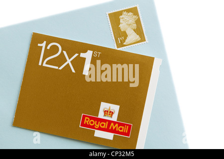 Book of twelve Royal Mail first class postage stamps and an envelope with a stamp isolated on a white background. England, UK Stock Photo