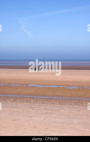 A COUPLE SIT ALONE ON THE VAST EXPANSE OF BRANCASTER BEACH. NORTH NORFOLK. UK. Stock Photo