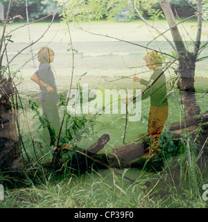 Two boys fishing at a beach double exposed with a forest on a lake Stock Photo