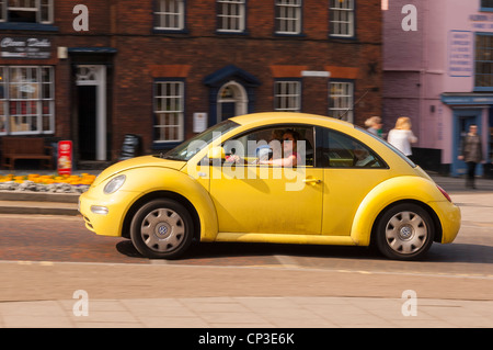 A yellow VW Beetle car driving through the city showing movement in Norwich , Norfolk , England , Britain , Uk Stock Photo