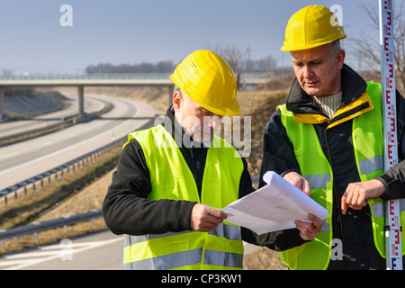 Land surveyors on highway reading geodesist plans use tacheometer Stock Photo