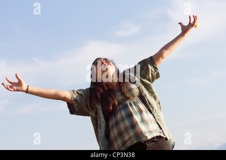 Cry out for joy - young teenage girl with raised arms feeling free. Sunny summer outdoor shot against a blue sky. Stock Photo