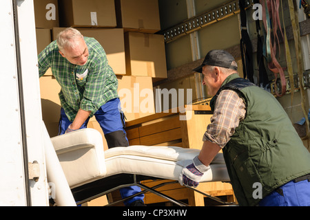 Two male movers putting furniture and boxes in moving truck Stock Photo