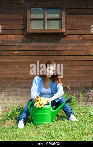 a woman sitting with a watering can in garden Stock Photo