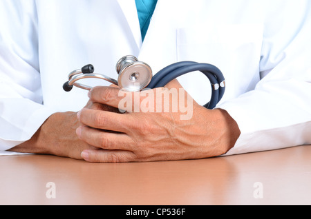 Closeup of a doctors hands holding a stethoscope on top of his desk. Stock Photo