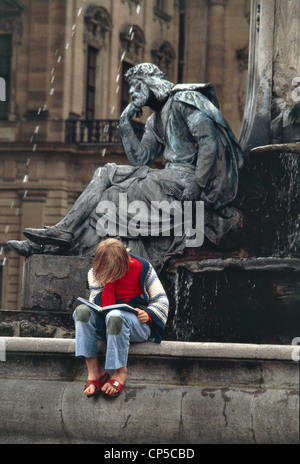 Germany - Bavaria - Wurzburg. A woman reading sitting on the fountain in front of the Franconian palace of the Prince Bishops. Stock Photo