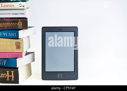 Kindle e-reader with a large pile of books. Stock Photo