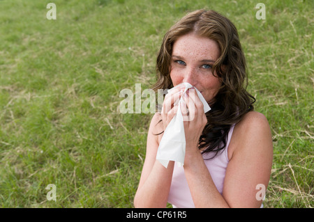 Germany, North Rhine Westphalia, Duesseldorf, Young woman sneezing in meadow, portrait Stock Photo