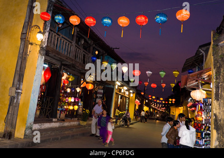 Horizontal of traditional souvenir shops open for business along a street in Hoi An decorated with lanterns lit up at night. Stock Photo