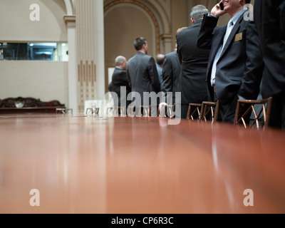 Businessmen inside a board room talk on mobile phones and chat with each other. Stock Photo