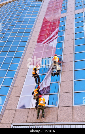 Workmen hanging a poster or billboard in sections on the side of a building in Wangfujing Street, Beijing, China Stock Photo