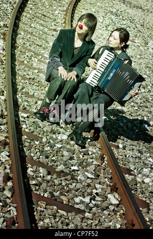 a sad clown couple sitting on railroad tracks - the woman plays the accordion Stock Photo