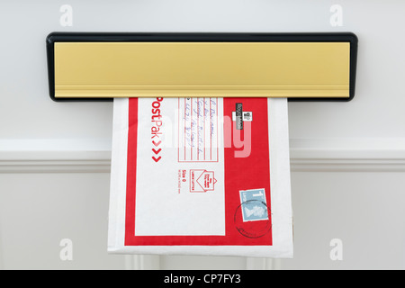 UK Royal Mail PostPak envelope with a large letter first class stamp posted through a letterbox flap in a white door at home. England Britain Stock Photo