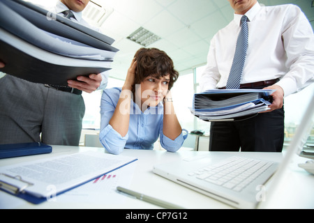 Terrified secretary touching her head while looking at big heaps of papers Stock Photo