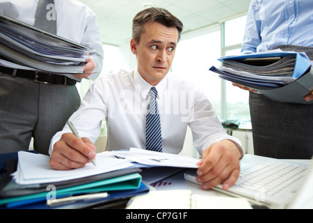 Shocked accountant looking at huge piles of documents while doing financial reports Stock Photo