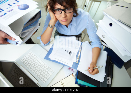 Perplexed accountant doing financial reports being surrounded by huge piles of documents Stock Photo