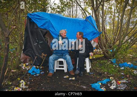 Two 'down and outs' drinking cheap wine and lager living in a makeshift tent in a disused Clyde dockyard, Glasgow. Stock Photo