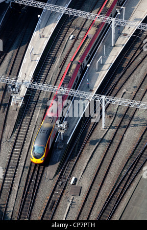 Bird's eye view of a train approaching a station, sidelit in the morning light.