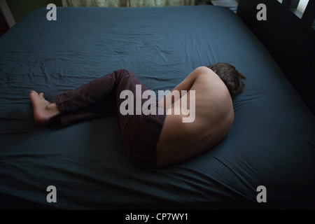 Twelve year old boy laying on a bed with a stomach ache. Stock Photo