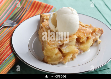 A piece of apple pie with a scoop of vanilla ice cream, on china plate on placemat with fork on a striped, colorful napkin.