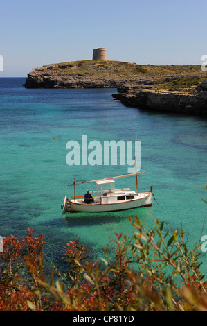 Small fishing boat, or llaut, moored in the inlet of Cala Alcaufar, Menorca, with the Matello Tower in the background Stock Photo