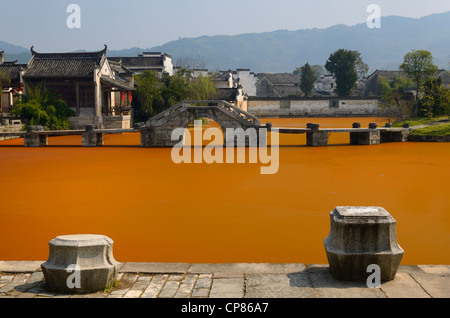 Stone moorings and bridge with bright red algae bloom scum on Longxi river in ancient Chengkan village Huangshan Peoples Republic of China Stock Photo