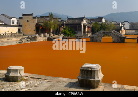 Stone moorings and bridge with bright red algae bloom scum on Longxi river in Chengkan village Huangshan Peoples Republic of China Stock Photo