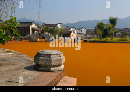 Stone steps and bridge with bright red algae bloom scum on Longxi river in Chengkan village Huangshan Peoples Republic of China Stock Photo