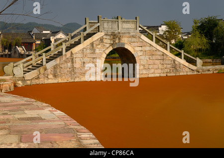 Stone bridge with bright red algae bloom scum on Longxi river in Chengkan village Huangshan Peoples Republic of China Stock Photo