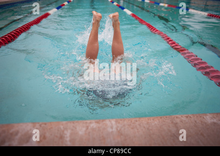 Boy standing upside down in a swimming pool, legs sticking up out of water. Stock Photo