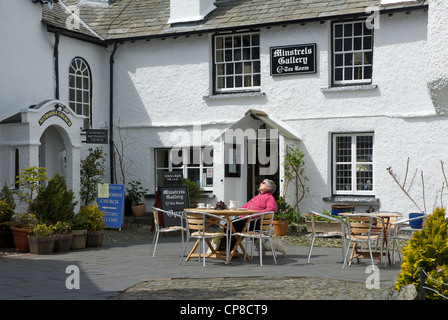 Woman relaxing outside the Minstrels Gallery Tea Room in the village of Hawkshead, Lake District National Park, Cumbria, UK