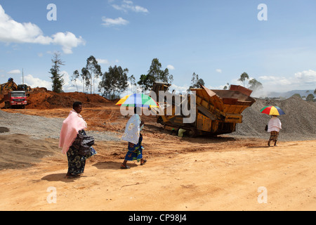 Women hold umbrellas to shade themselves from the sund and walk along a highway in the Western Province of Rwanda. Stock Photo