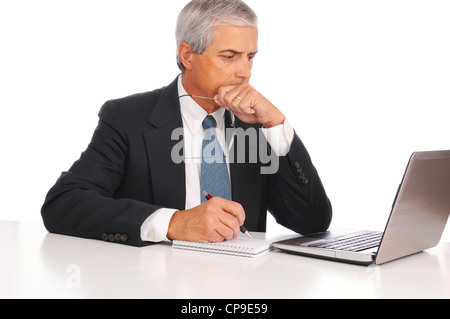 Smiling Middle Aged Businessman at desk using laptop computer with concerned expression isolated on white. Stock Photo