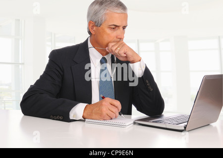 Smiling Middle Aged Businessman at desk using laptop computer with concerned expression in modern office. Stock Photo