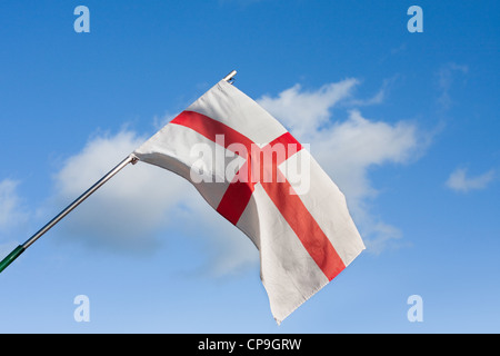Slighted tattered English flag hanging from mast against blue sky Stock Photo