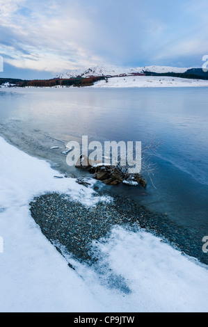 A frozen Clatteringshaws Loch with Craignell in the distance in winter, Galloway Forest Park, Galloway, Scotland, UK Stock Photo