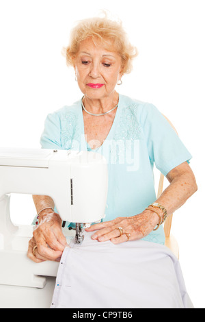 Elderly woman sews with her sewing machine. Isolated on white. Stock Photo
