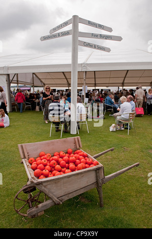 Visitors in refreshment area at show, wheelbarrow of tomatoes & sign directing people to choice of food outlets - Tatton Park RHS Flower Show, GB, UK.