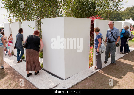 People peering in & viewing 'The Kaleidoscope' garden through gap in boundary wall (white panels) - RHS Flower Show, Tatton Park, Cheshire, England. Stock Photo