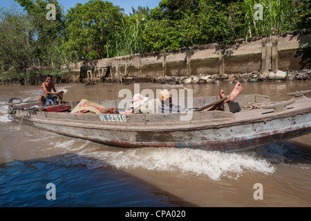 Vietnamese men travelling in a long boat, between Cai Be and Vinh Long, Mekong River Delta, Vietnam Stock Photo