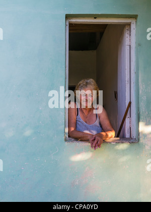 A 60-70 year old Cuban woman looks out of her window and leans her arms on the window sill in Viñales, Cuba. Stock Photo