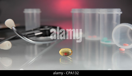 pills of various colors in plastic containers, a stethoscope and a gel pill on reflective table Stock Photo