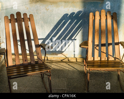 Long shadows cast by two chairs made with wooden slats placed on the front porch of a Cuban house in Viñales, Cuba. Stock Photo