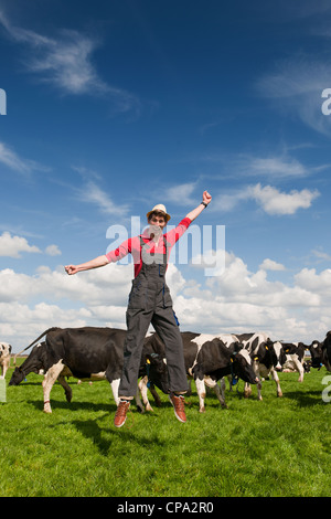 Happy young farmer jumping in field with cows Stock Photo