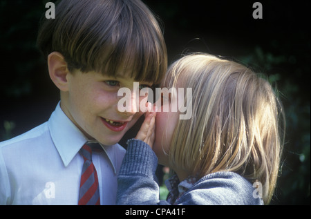 little girl whispering into boy's ear Stock Photo